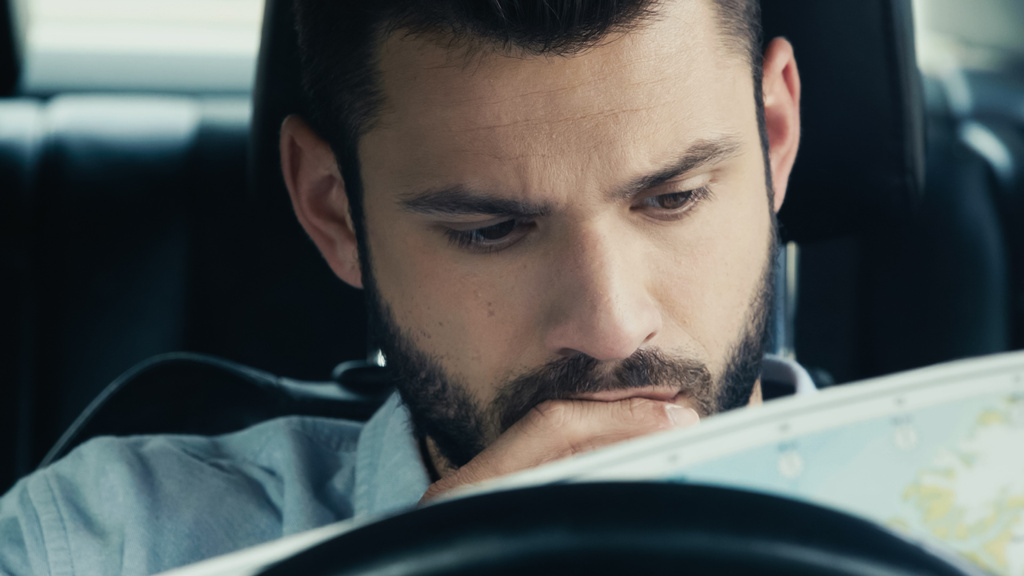 pensive man looking at map while sitting in car and estimating route - Фото, изображение