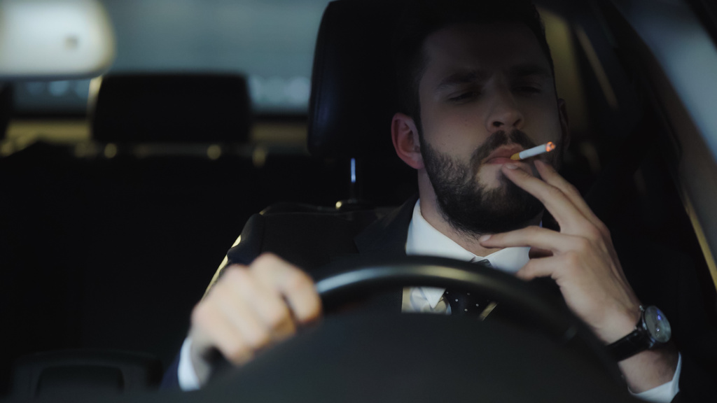 bearded businessman smoking cigarette while driving auto at night - 写真・画像