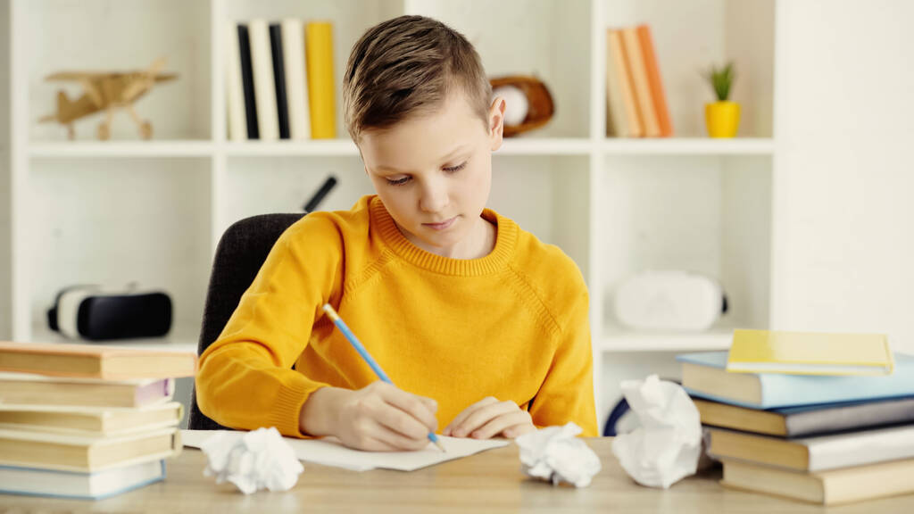 preteen schoolboy drawing near crumpled papers and books on desk  - Fotó, kép