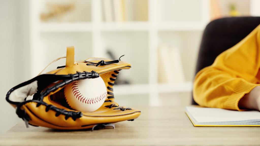 baseball glove with ball near schoolkid doing homework at desk  - Foto, Imagen
