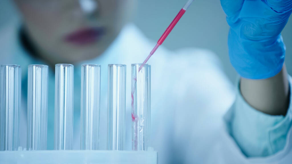 partial view of blurred scientist adding red sample into clean test tube in laboratory  - Фото, изображение