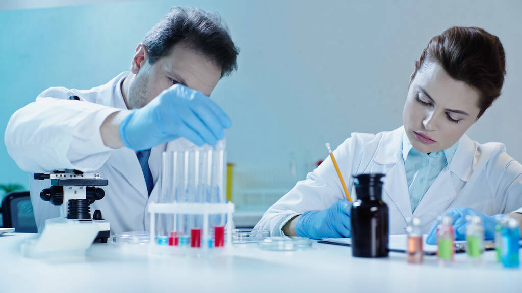 scientist taking test tube with sample near colleague writing in laboratory - Фото, изображение