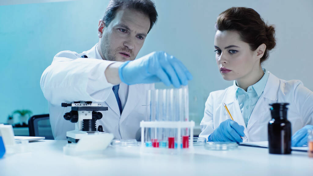 scientist taking test tube with sample near colleague with pencil in lab - Foto, Bild