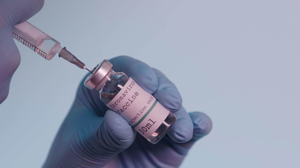 cropped view of scientist in latex gloves filling in syringe with vaccine from bottle with lettering isolated on grey  - 写真・画像