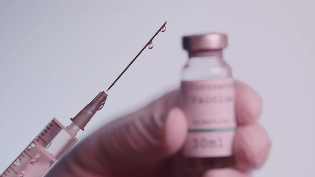 обрізаний вид вченого, який тримає шприц і розмиту пляшку з вакциною ізольовано на сірому
  - Фото, зображення