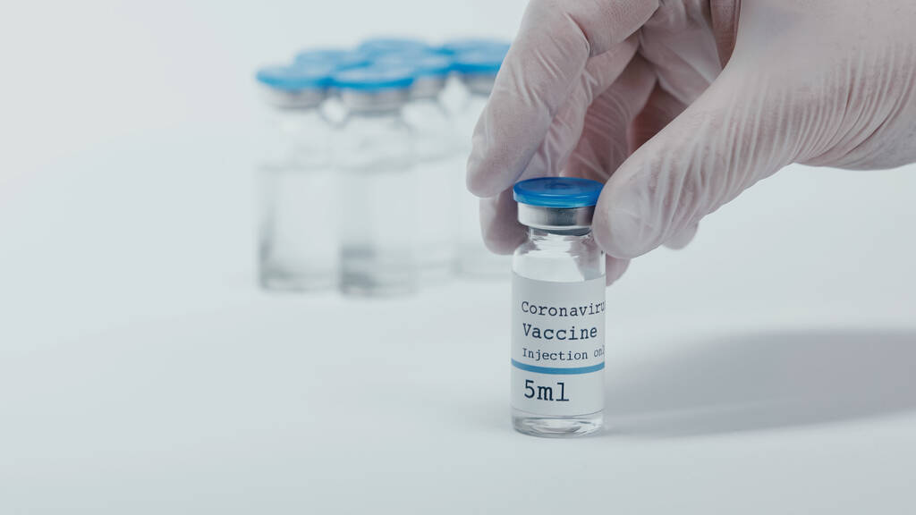 cropped view of person holding bottle with coronavirus vaccine liquid on white  - Photo, image