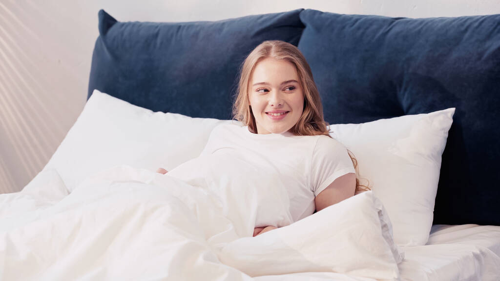 Smiling woman looking away while lying on bed in morning  - Photo, Image