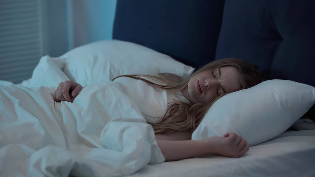 Неспокійна жінка з закритими очима лежить на ліжку вдома
  - Фото, зображення