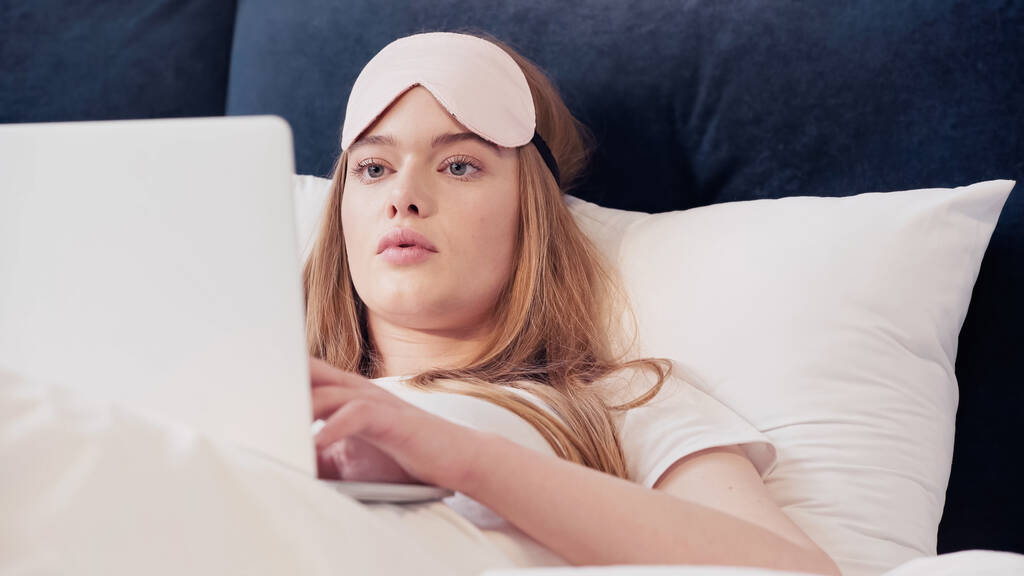 Freelancer in sleep mask using laptop on bed in morning  - Foto, afbeelding