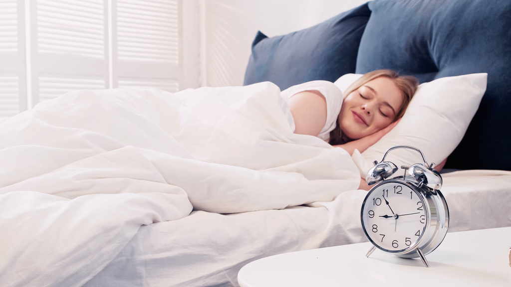 Smiling woman lying on bed near alarm clock in morning  - Photo, image