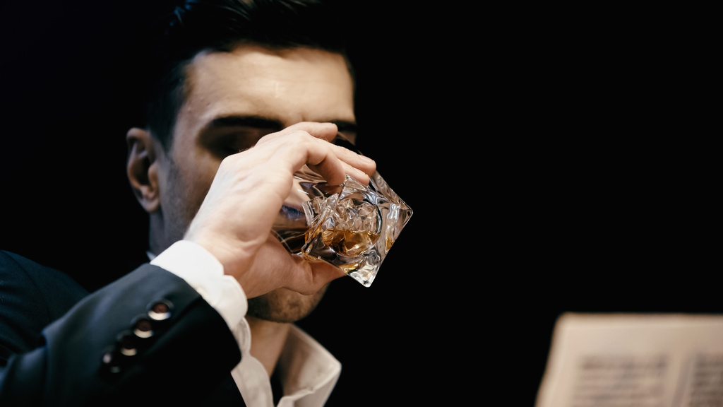 Businessman in formal wear drinking whiskey near blurred newspaper isolated on black  - Zdjęcie, obraz