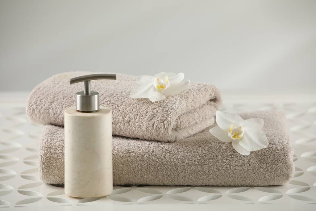 Soft folded towels, orchid flowers and dispenser on white table - Fotó, kép