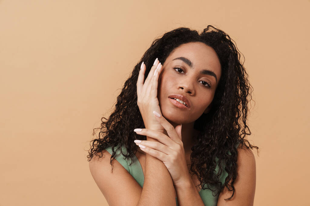 Young black woman touching her face and looking at camera isolated over beige background - Foto, afbeelding