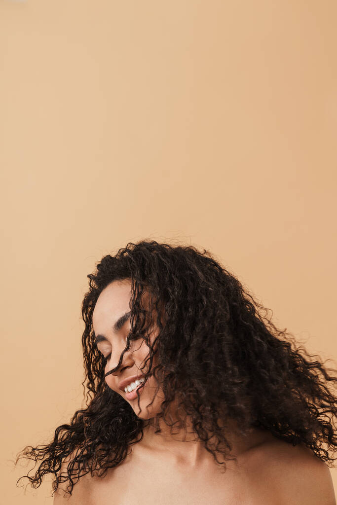 Shirtless black woman laughing while making fun with her hair isolated over beige background - Zdjęcie, obraz