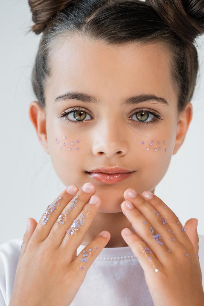 portrait of adorable girl with sparkling glitter stars on face and hands looking at camera isolated on grey - Fotografie, Obrázek