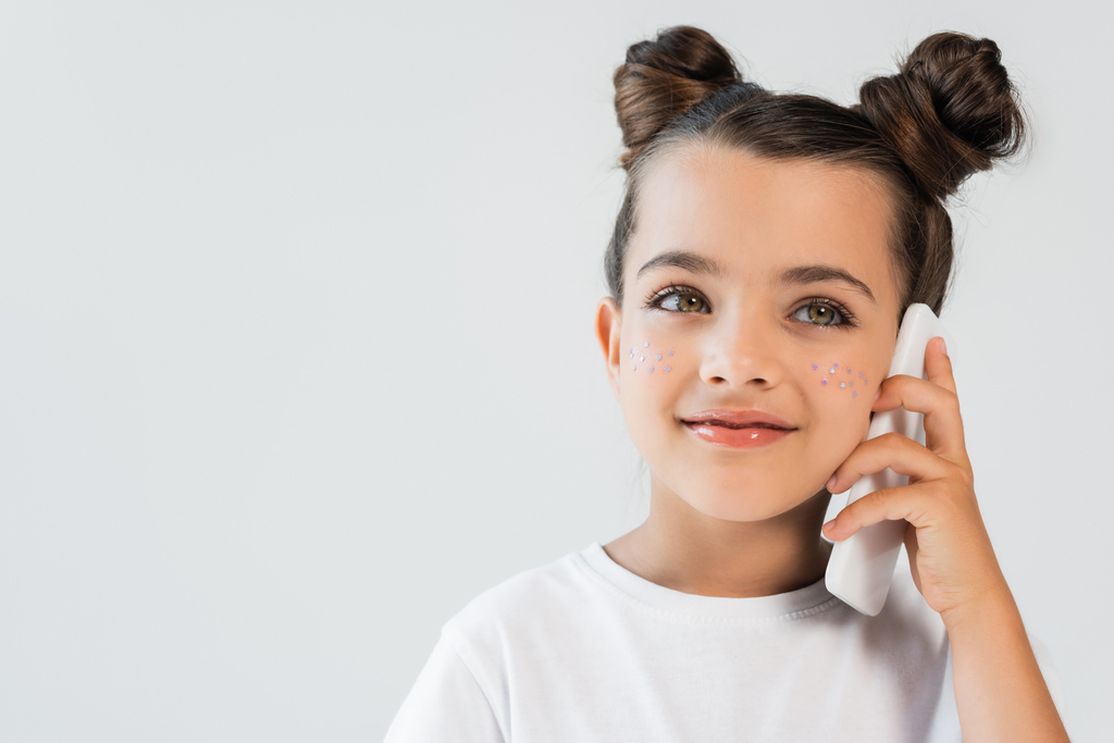 smiling girl with glitter stars on cheeks talking on mobile phone isolated on grey - Foto, immagini