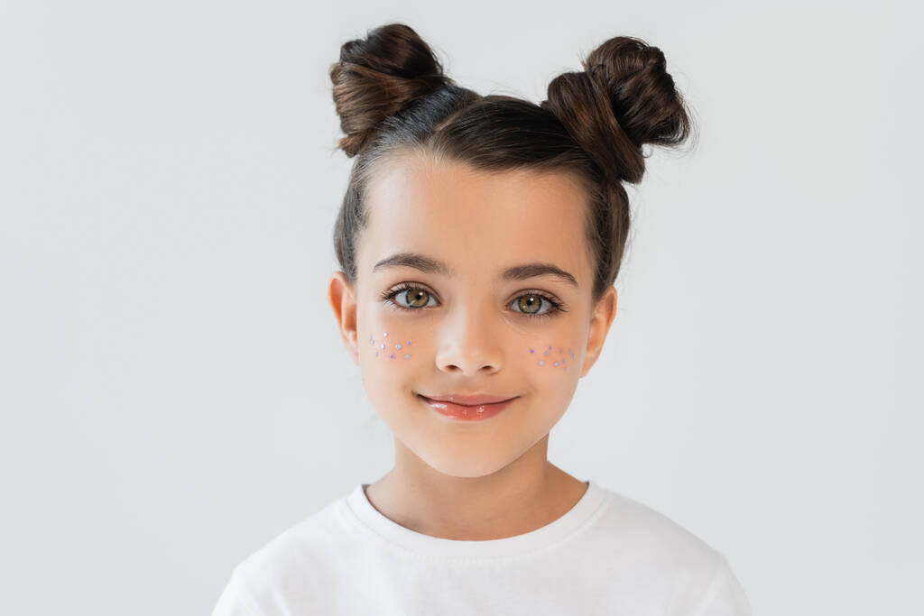 portrait of cheerful child with lip gloss and glitter stars on cheeks looking at camera isolated on grey - Fotografie, Obrázek