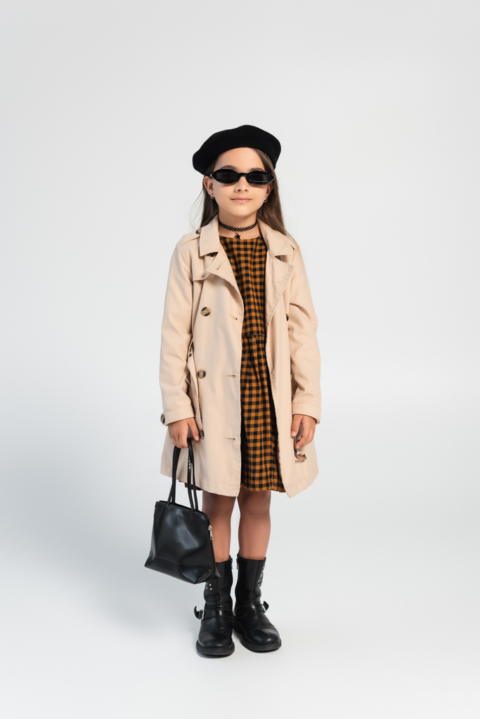 full length of stylish girl in trench coat and beret holding handbag on grey - Valokuva, kuva