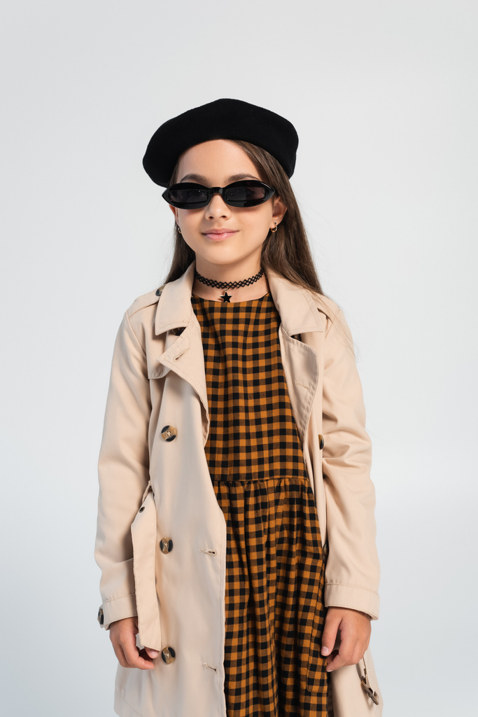 stylish girl in trench coat, beret and sunglasses smiling isolated on grey - Photo, Image
