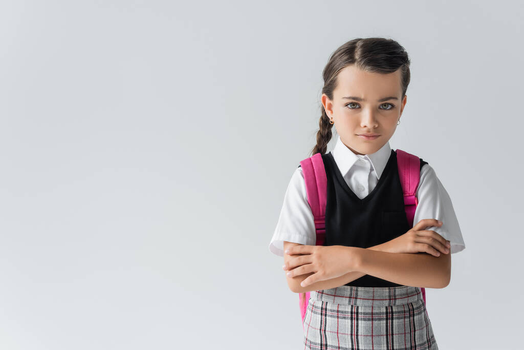 sad schoolgirl with backpack standing with crossed arms isolated on grey - Foto, Bild