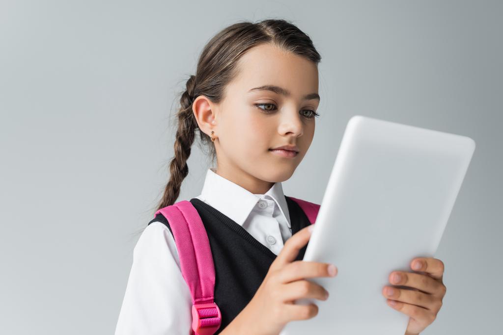 мила дівчина в шкільній формі з рюкзаком за допомогою цифрового планшета ізольована на сірому
 - Фото, зображення