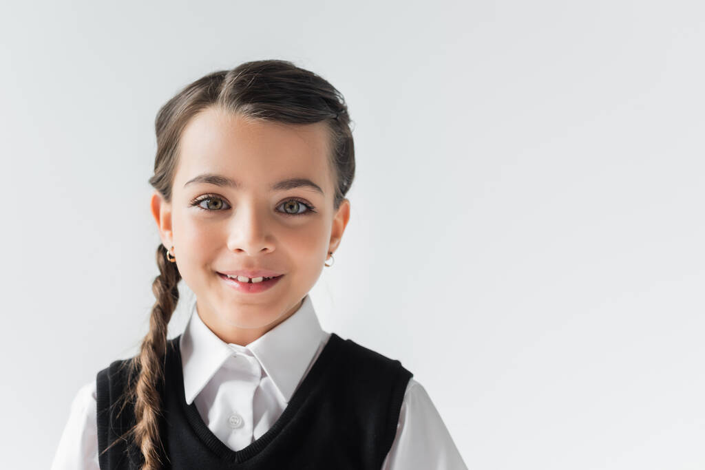portrait of happy schoolgirl in white shirt and vest looking at camera isolated on grey - Foto, Imagem