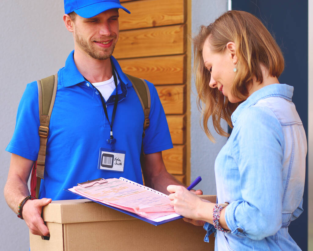 Repartidor sonriente con uniforme azul que entrega la caja de paquetes al destinatario: concepto de servicio de mensajería. Repartidor sonriente en uniforme azul. - Foto, Imagen