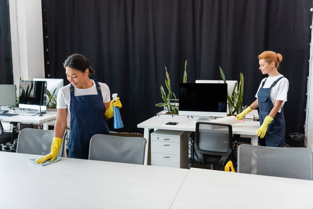 interracial femmes avec chiffon et brosse à poussière bureaux de nettoyage dans le bureau - Photo, image