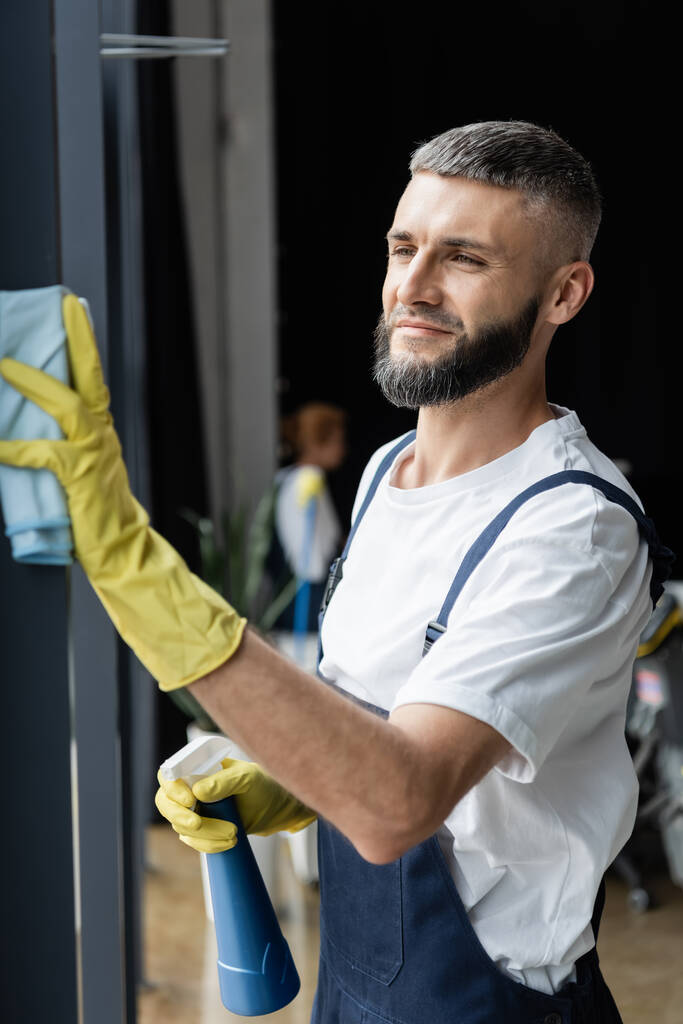 ufficio pulizia uomo barbuto sorridente con detersivo e straccio - Foto, immagini