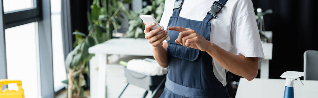 cropped view of professional cleaner in overalls pointing at mobile phone, banner - Photo, Image