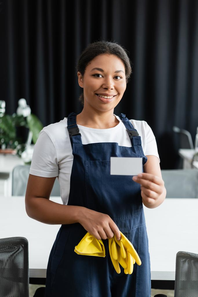 bonita mujer bi-racial en uniforme con guantes de goma y tarjeta de visita en blanco - Foto, imagen