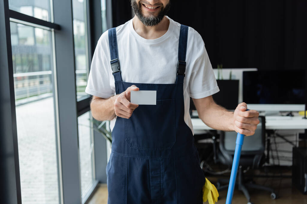 gedeeltelijke weergave van een glimlachende man in een overall met blanco visitekaartje - Foto, afbeelding