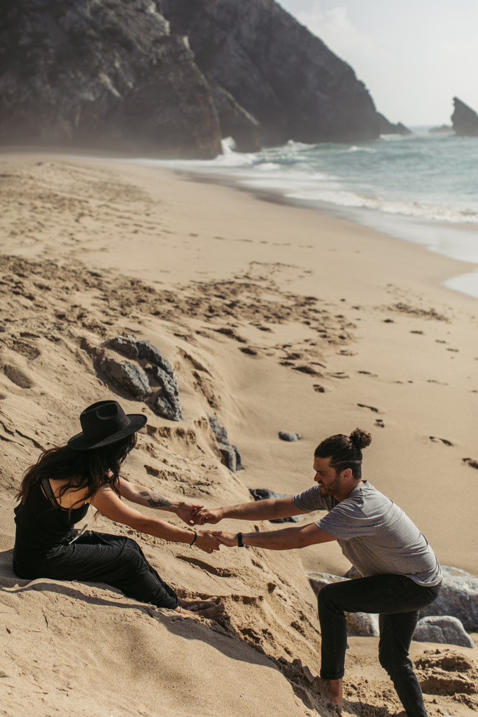 bearded man holding hands with tattooed girlfriend in dress and hat on beach in portugal  - Photo, Image