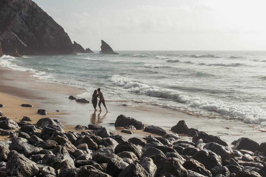 barbudo hombre abrazando novia en vestido mientras caminando en océano agua  - Foto, imagen