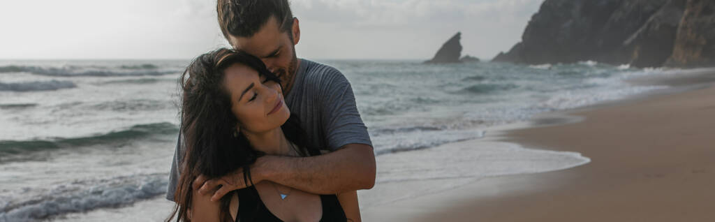 ポルトガルの海の近くで笑顔の彼女を抱きしめる幸せな男バナー - 写真・画像