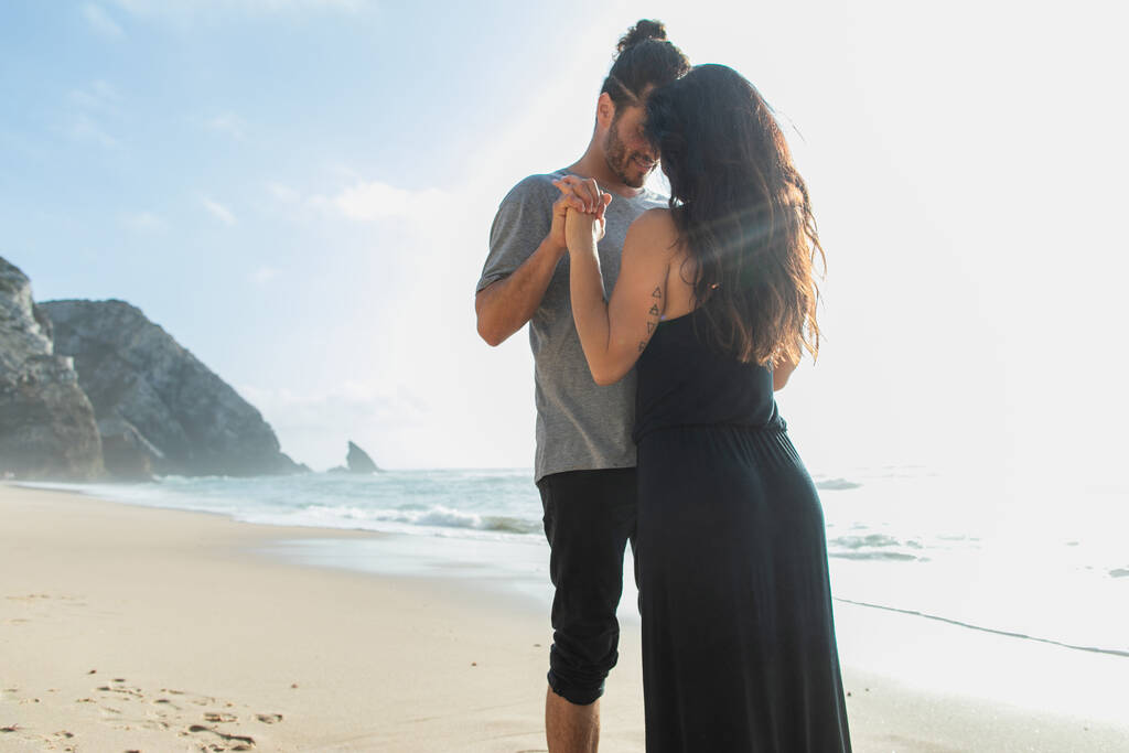 Mutlu sakallı adam tatilde okyanus kenarında esmer kız arkadaşıyla el ele tutuşuyor.  - Fotoğraf, Görsel