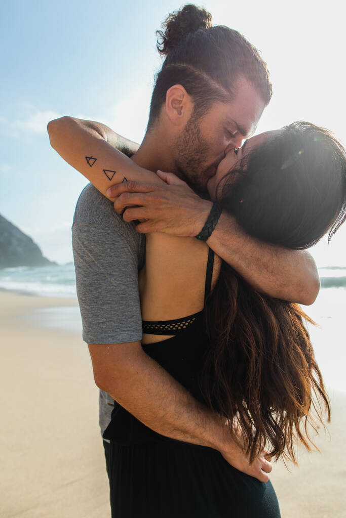 bearded man kissing with tattooed girlfriend near ocean in portugal  - Photo, Image