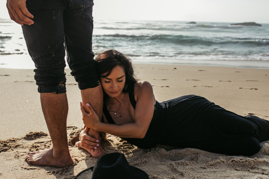mujer en vestido acostado sobre arena mojada y abrazo pierna de novio cerca del océano  - Foto, Imagen