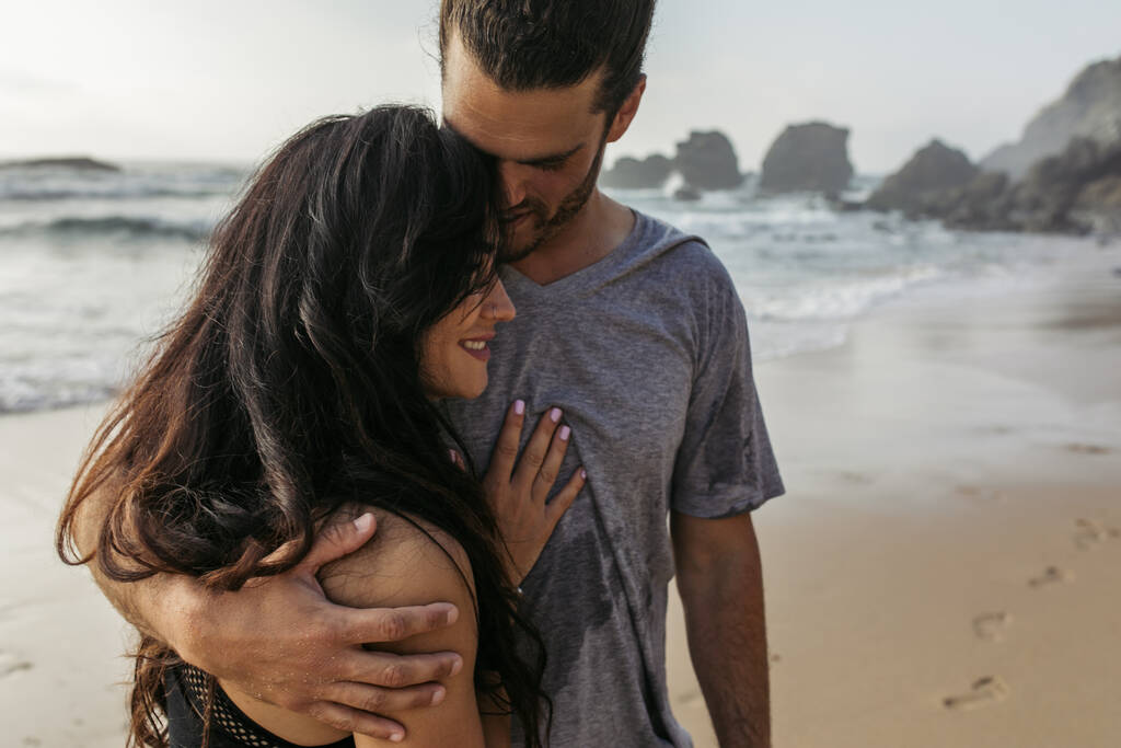 vousatý muž v šedém tričku objímající šťastný přítelkyně v blízkosti oceánu v portugalštině - Fotografie, Obrázek