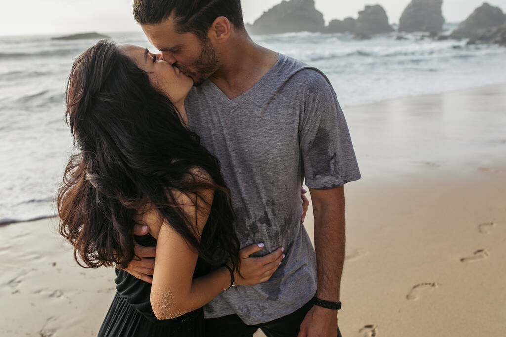 bärtiger Mann im grauen T-Shirt küsst Freundin am Meer in Portugal - Foto, Bild