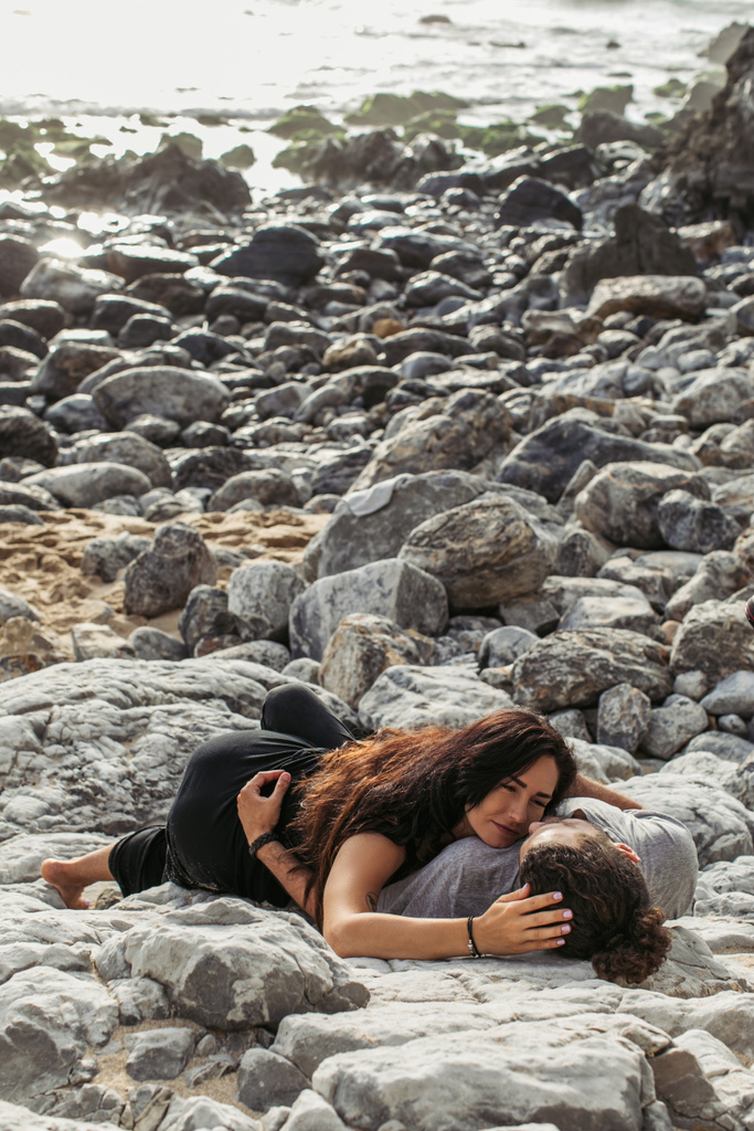 Dövmeli kadın ve erkek birlikte okyanusun yakınındaki taşlarda yatıyor.  - Fotoğraf, Görsel