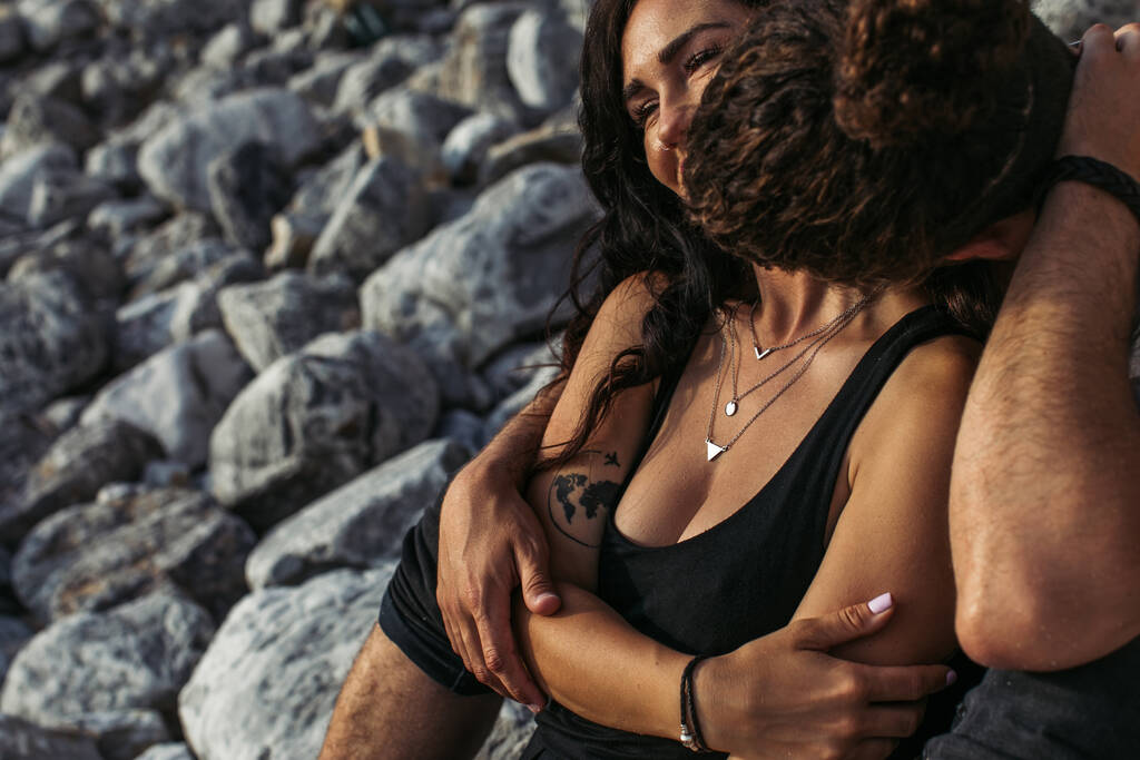 férfi csók tetovált barátnő ruha közelében sziklák a strandon - Fotó, kép