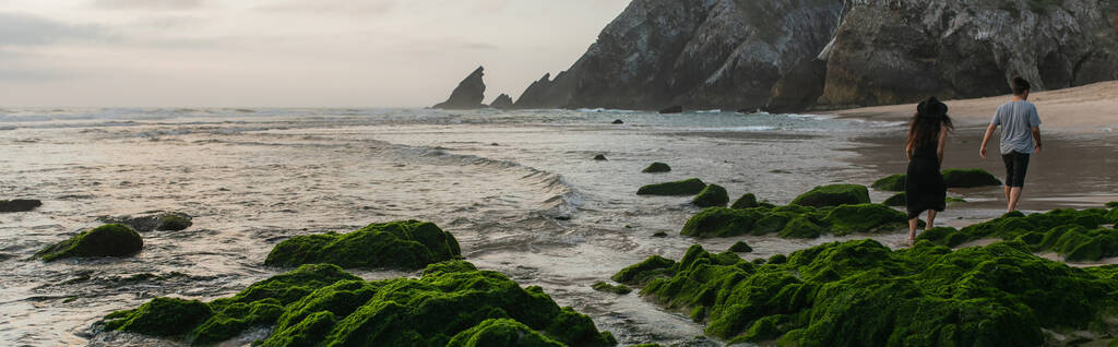 вид ззаду пари, що ходить біля зелених мохоподібних каменів в океані під час заходу сонця, банер
 - Фото, зображення