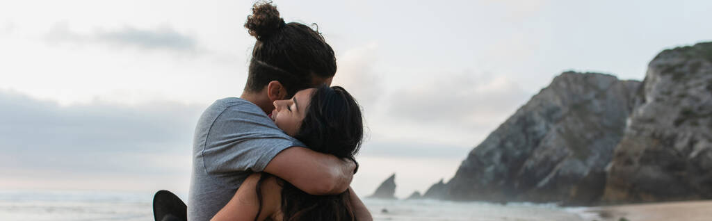 homme et femme brune avec les yeux fermés étreignant sur la plage en portugais, bannière - Photo, image