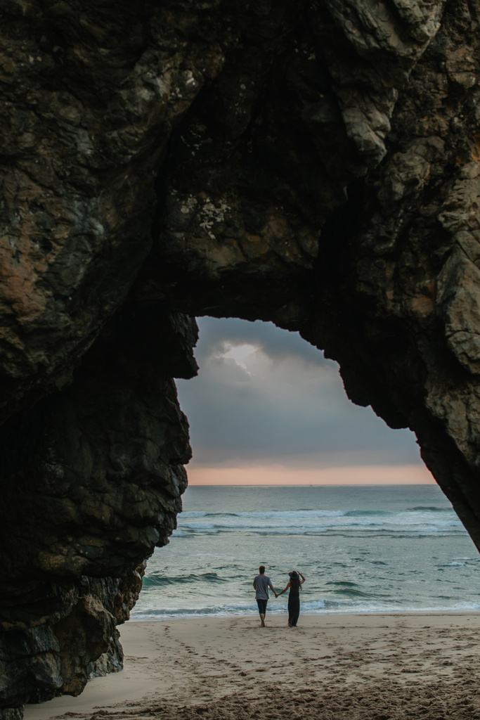 achteraanzicht van paar hand in hand staan op het strand tijdens zonsondergang  - Foto, afbeelding