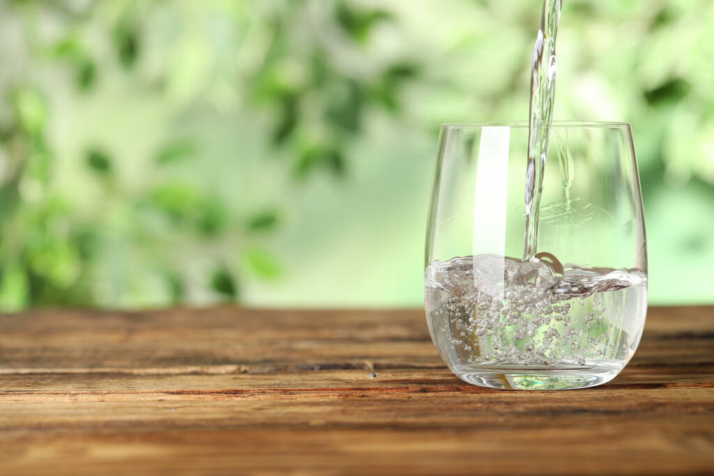 Pouring water into glass on wooden table outdoors, space for text. Refreshing drink - 写真・画像