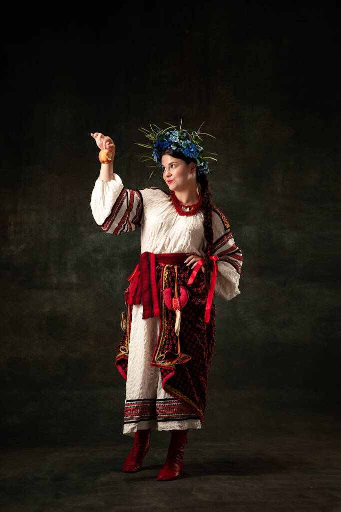 Freedom and independence. Art portrait of beautiful woman wearing traditional folk Ukrainian costume posing isolated over dark vintage background. Fashion, beauty, cultural heritage concept. - Foto, imagen