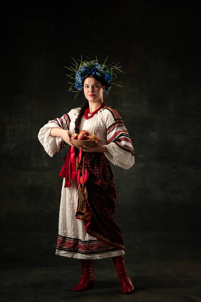 Apples. Emotional adorable woman wearing national folk Ukrainian attire posing isolated over dark vintage background. Fashion, beauty, cultural heritage concept. - Foto, immagini