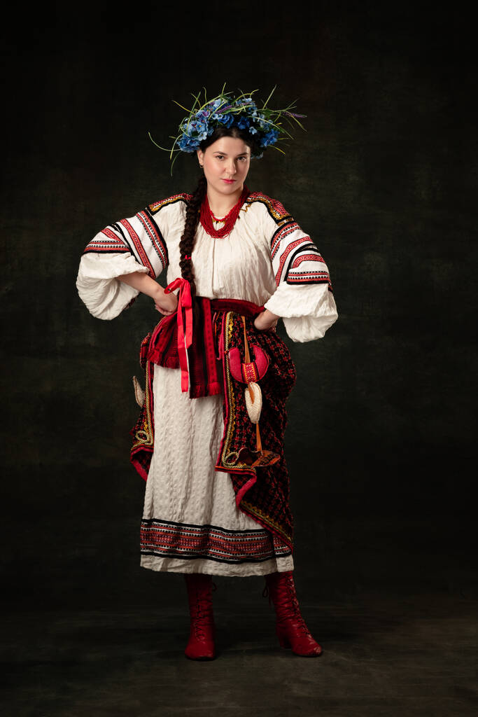 Freedom and independence. Art portrait of beautiful woman wearing traditional folk Ukrainian costume posing isolated over dark vintage background. Fashion, beauty, cultural heritage concept. - Zdjęcie, obraz