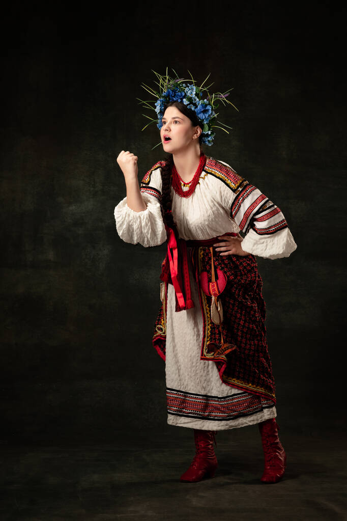 Figth for rights. Emotional adorable woman wearing national folk Ukrainian attire posing isolated over dark vintage background. Fashion, beauty, cultural heritage concept. - Фото, зображення